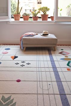 a white rug with colorful designs on it in front of a window and potted plants