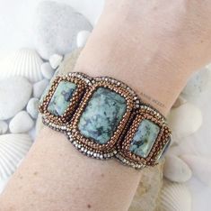 a woman's hand wearing a beaded bracelet with blue and brown stones on it