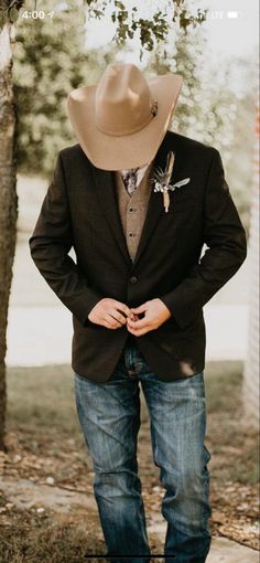 a man wearing a cowboy hat standing in front of a tree with his hands on his hips