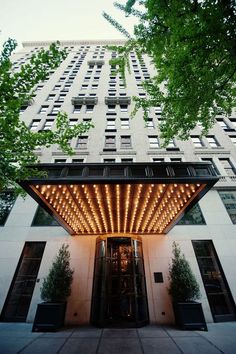 the entrance to an apartment building with lights on it's sides and trees in front