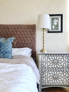 a bed with white sheets and pillows next to a lamp on top of a dresser