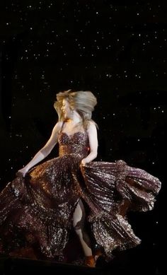 a woman in a long dress is walking on stage with her hair blowing in the wind