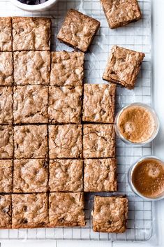 someone is holding their hand over some brownies on a cooling rack with two cups of coffee