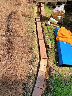 a blue bench sitting in the grass next to a brick wall and some dirt on the ground