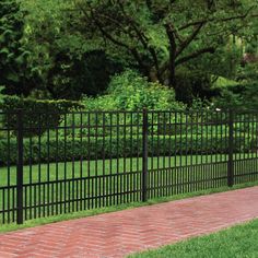 a black fence and brick walkway in front of some green grass with trees behind it