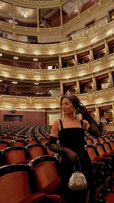 a woman standing in front of an empty auditorium with red chairs and chandeliers