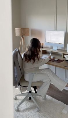 a woman sitting at a desk in front of a computer on top of a white rug