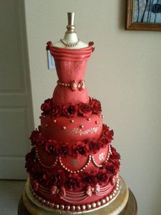 a three tiered cake with red flowers and pearls on the top, sitting on a table