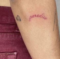 a woman with a tattoo on her arm that says paradise in cursive writing