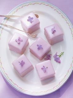 four square pieces of pink cake on a plate with purple flowers and a spoon in the middle