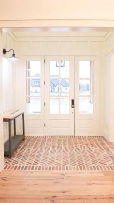 an empty entryway with two doors and a bench in the center, on a wooden floor