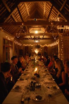 a group of people sitting at a long table with food and candles in front of them