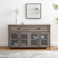 a wooden cabinet with glass doors and drawers in front of a white brick wall next to a potted plant