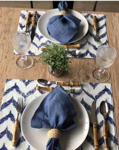 a place setting with blue napkins, silverware and a potted plant on the table