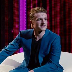 a man sitting on top of a white chair in front of a purple and red wall