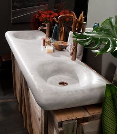 a white sink sitting on top of a wooden table next to a potted plant