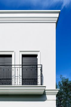 two windows on the side of a white building with black shutters and balconies