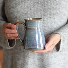 a woman holding a blue and white coffee mug in her right hand while wearing a gray sweater