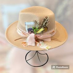 The Bentley is ready for that concert or church. It has a pink base with a twisted tie dye chiffon wrapped around and tied. Then it is double wrapped in tan leather.  Tucked behind the band is a few feathers and flowers.  Then tied together with a burnt edged card displaying The Great Sand Dunes.  So elegant but edgy.   This hat is tan and fedora style.  Head circumference is 56-58 cm and can be adjusted on the inside with a tie.  The brim measures 2.95 inches and made of 65% cotton and 35% polyester.   Each hat from The Bandit Hat Co has been customized with my own personal touch.  Each hat that has been created is unique and there will never be two the same. Adjustable Felt Hat For Country Summer Events, Adjustable Felt Hat For Summer Country Events, Adjustable Summer Felt Hat For Country Events, Adjustable Country Style Felt Hat For Summer, Fitted Wide Brim Felt Hat For Spring, Spring Fitted Wide Brim Felt Hat, Fitted Cream Fedora For Spring, Adjustable Felt Hat For Kentucky Derby, Adjustable Hat Bands For Country Events In Spring