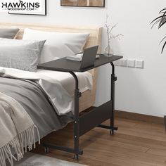 a laptop computer sitting on top of a wooden desk next to a bed with white sheets