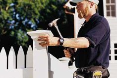 a man is holding a hammer and working on a white picket fence with his hands