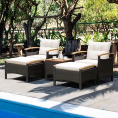 four wicker lounge chairs sitting next to a swimming pool with trees in the background