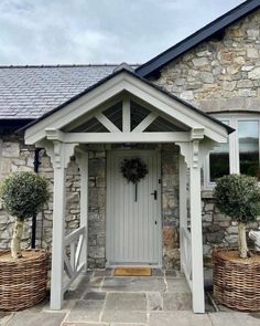 the front entrance to a stone house with potted plants and baskets on either side