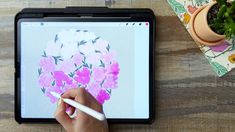 a person is drawing flowers on a tablet with a white pen and potted plant in the background