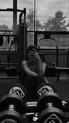 a woman sitting on top of a bench next to some dumbbells in a gym