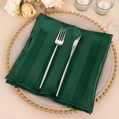 a place setting with green napkins, silverware and flowers on a table cloth