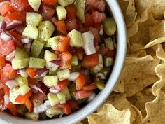 a white bowl filled with chopped vegetables next to tortilla chips on top of a table