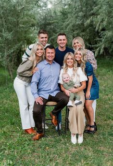 a family posing for a photo in the grass with trees behind them and one man holding a baby