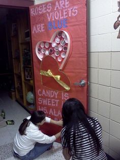 two girls are decorating a valentine's day door