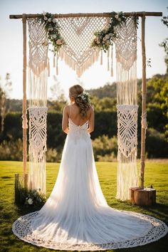 the back of a bride's dress standing in front of an outdoor wedding arch