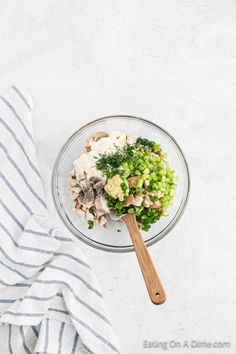 a glass bowl filled with chopped vegetables on top of a white surface next to a wooden spoon