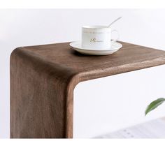 a white coffee cup sitting on top of a wooden table next to a green plant