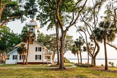 a white house sitting on top of a lush green field next to the ocean and trees