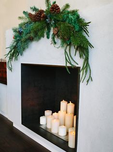 candles are lit in front of a fireplace decorated with greenery and pine cones on the mantle