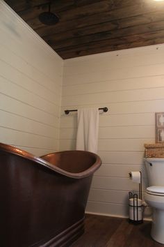 a bathtub and toilet in a bathroom with white walls, wooden floors and wood paneling