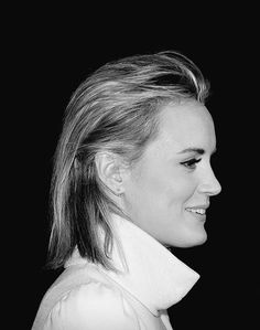 a black and white photo of a woman with her hair in a pony tail, smiling