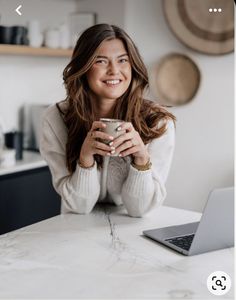 a woman sitting at a kitchen counter holding a cup