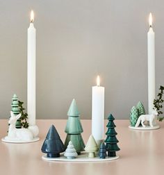 candles are lined up on a table next to small christmas trees