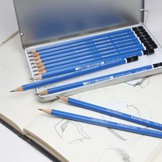 several blue pencils in a metal case on top of an open book with drawings