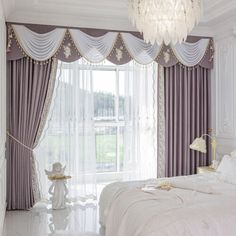 a white bed sitting under a chandelier in a bedroom next to a window