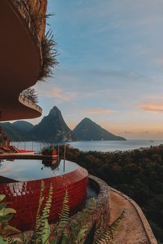 an outdoor swimming pool surrounded by greenery and mountains in the distance with water running through it