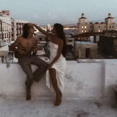 a man and woman sitting on top of a building next to each other