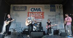 three men on stage with guitars and microphones in front of a large sign that says cma music festival