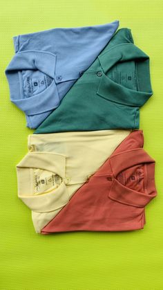 four different colored shirts laid out on a green surface with one folded up and the other unbuttoned