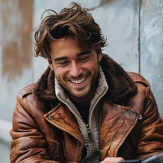 a smiling man wearing a brown jacket and holding a cell phone in his right hand