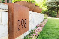 a house number sign on the side of a stone wall with flowers growing out of it